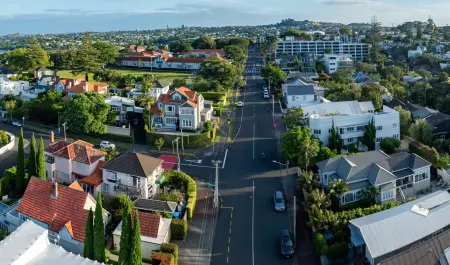 The photo shows houses, trees, and cars on the road. The image captures the urban landscape of Auckland.