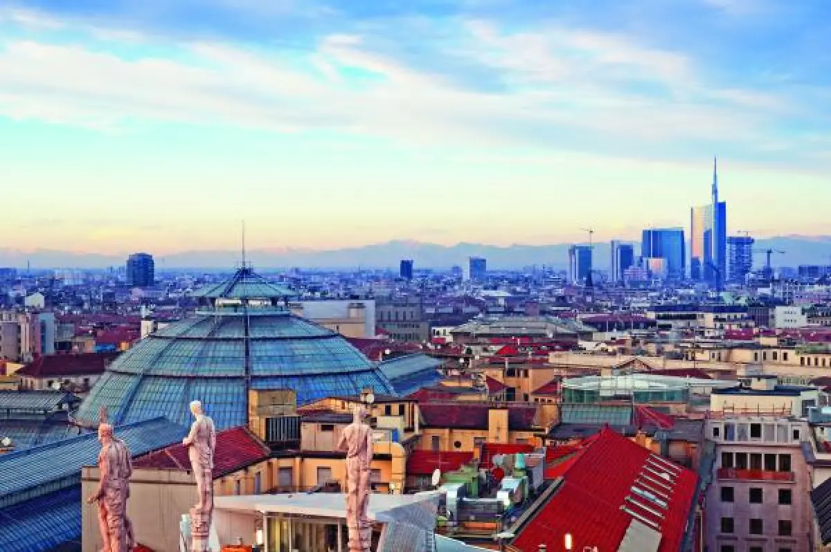 Red-tiled rooftops, stone statues on a rooftop terrace, a large glass-domed building at center, and a modern skyline with tall skyscrapers in the distance.