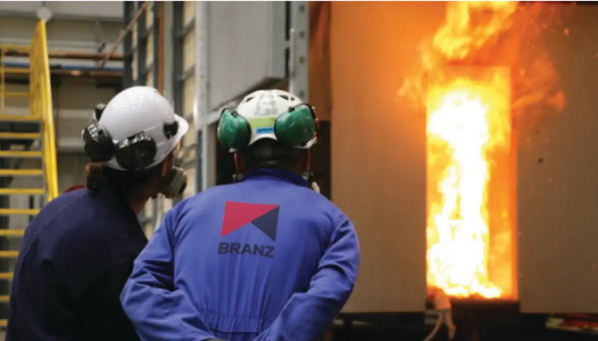 Photograph showing two people in protective clothing observing a wall opening with flames burning inside