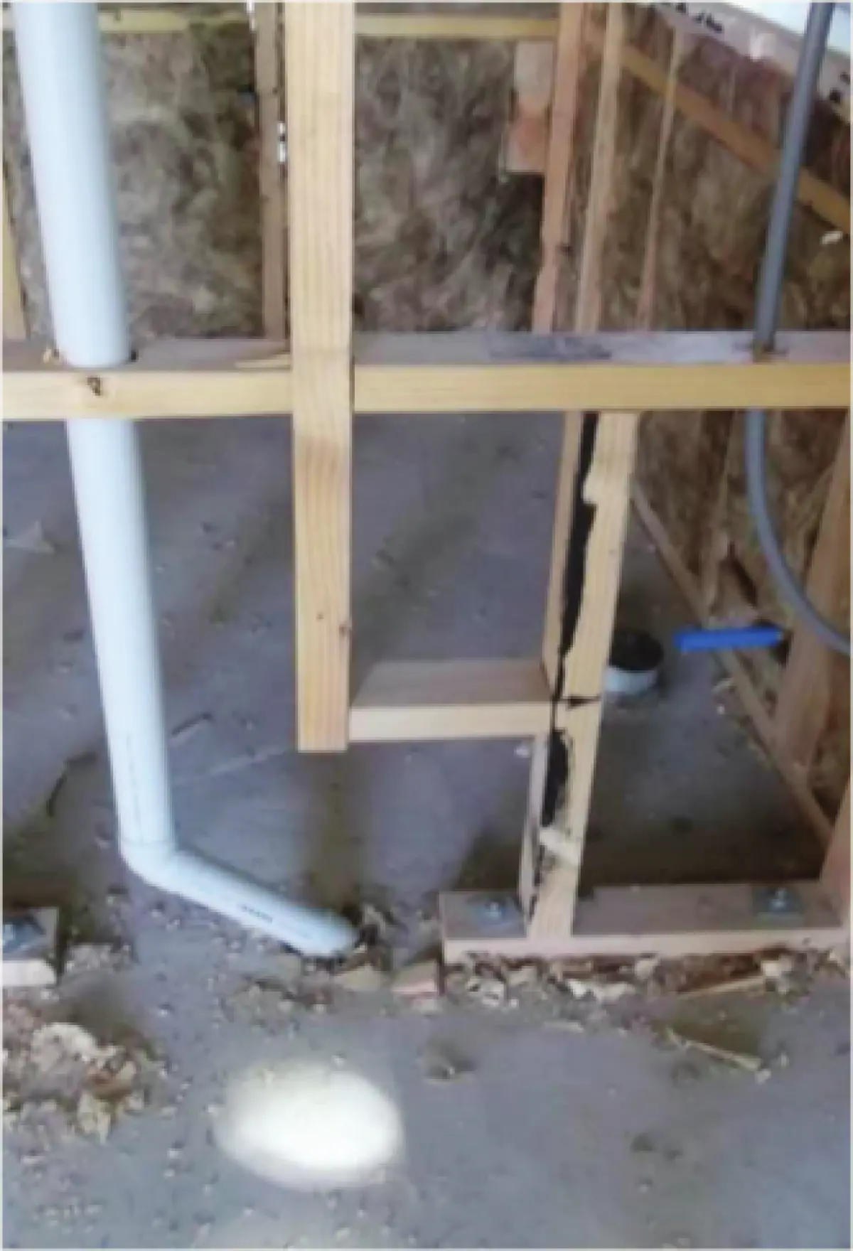 Photograph showing timber wall framing with insulation between studs and exposed plumbing pipes running through the wall cavity