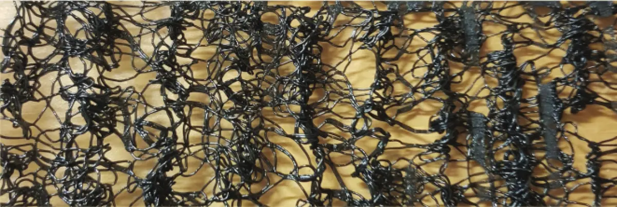 Photograph showing a close‑up of a black plastic mesh material laid over a yellow surface