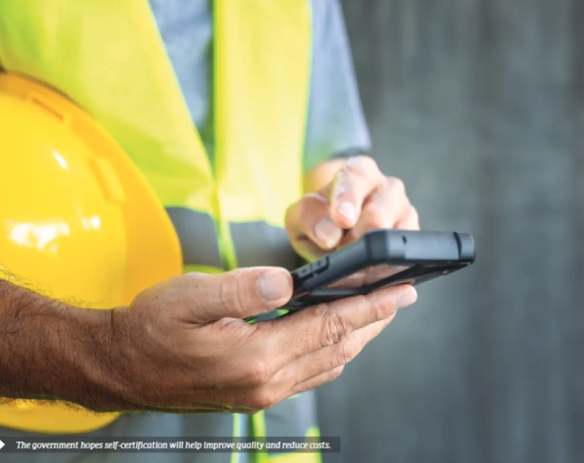 Photograph showing a person holding a smartphone while wearing a high‑visibility vest and holding a safety helmet