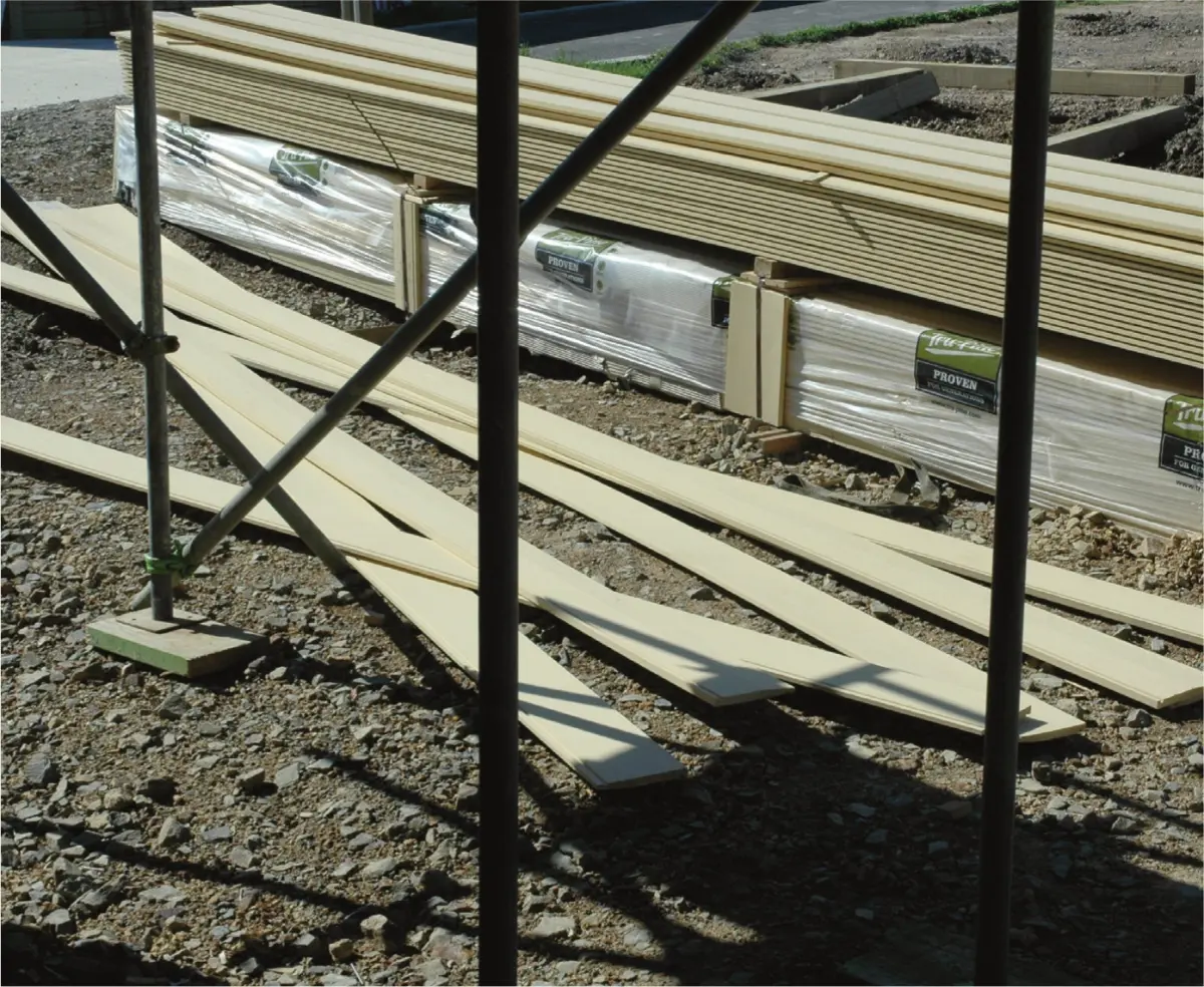 Stacked timber boards and wrapped building materials left on the ground at a construction site