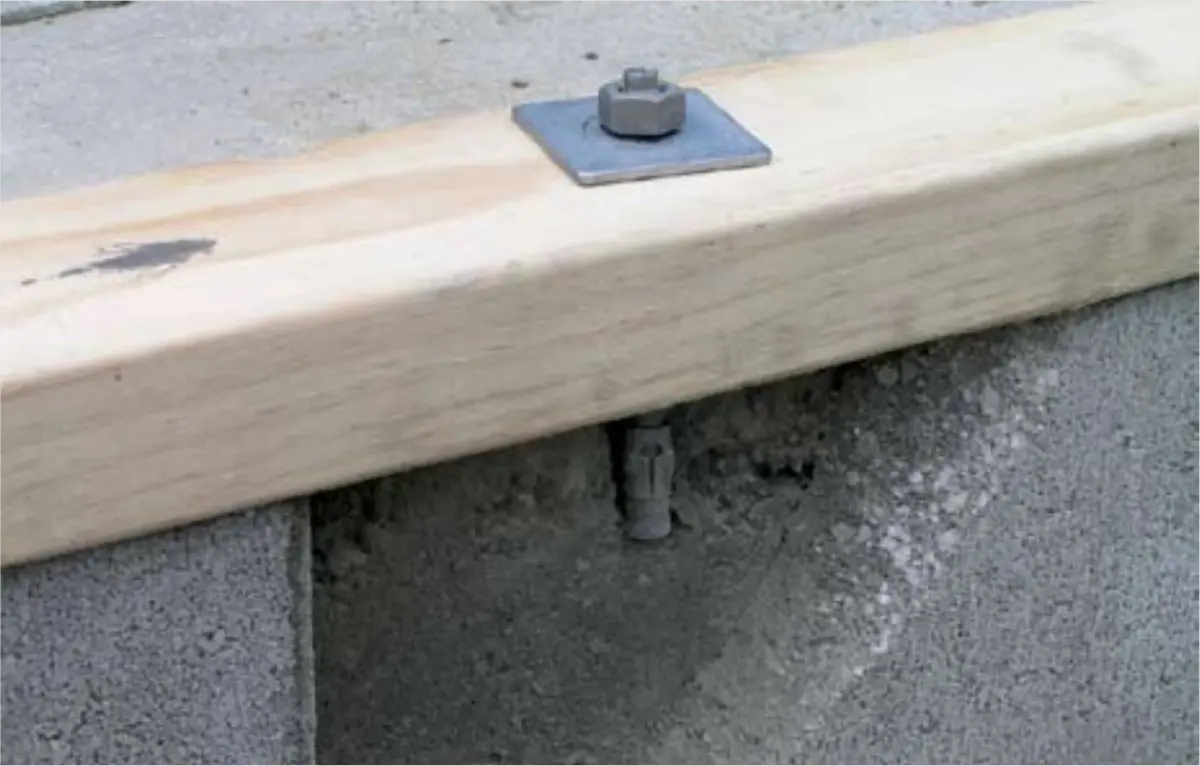 a photo of A bolt going through a wooden frame into a concrete slab but the slab has a piece missing making the bolt useless