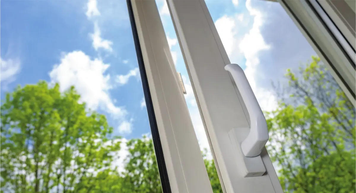 Photograph showing a close‑up of a uPVC‑framed window handle on a white window frame, with trees and sky visible through the glass
