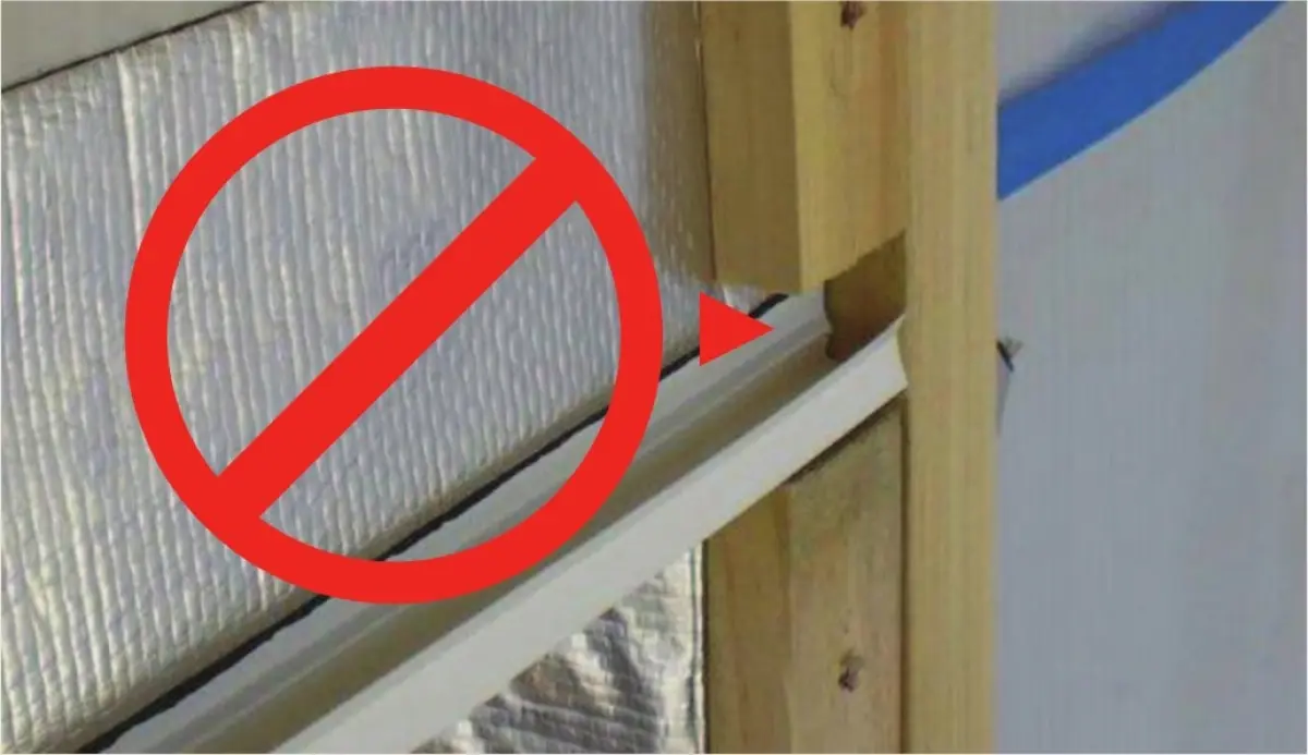Photograph showing a close‑up of wall framing with reflective wall wrap, a horizontal trim piece at the edge, and a red ‘do not’ symbol over part of the detail