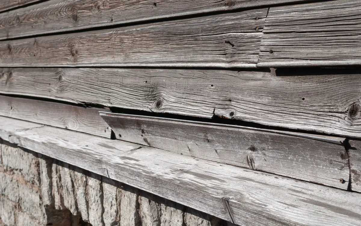 An image of old wooden house facade with warped weathered boards and peeling surface.